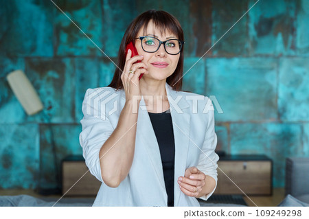 Mature business woman talking on mobile phone in office Mature business woman talking on mobile phone in office 109249298