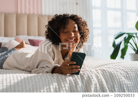 African girl holding smartphone touch screen typing scroll page at home. Woman with cell phone surfing internet using social media apps playing game. Shopping online Internet news cellphone addiction African girl holding smartphone touch screen typing scroll page at home. Woman with cell phone surfing internet using social media apps playing game. Shopping online Internet news cellphone addiction 109250033