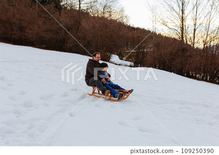 father and child together on wooden sled going down the snowy hill father and child together on wooden sled going down the snowy hill 109250390