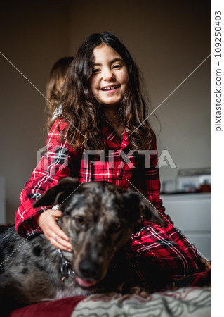 smiling girl in checked pajamas hugging her grey dog 109250403