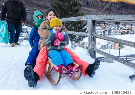 father with three daughters going down on snow slope with wooden sled 109250421