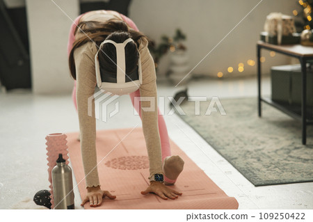 A lovely, sporty lady doing her stretches while wearing a virtual reality headset. 109250422