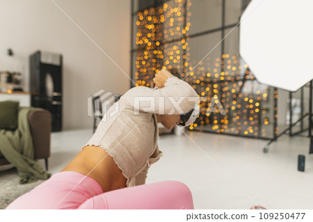 Engaging in fitness routines in a pink athletic attire while wearing a virtual reality headset near a Christmas tree. Engaging in fitness routines in a pink athletic attire while wearing a virtual reality headset near a Christmas tree. 109250477