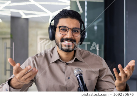 Webcam view, man in headphones looking at camera, smiling, using professional microphone to record podcast training online video course, businessman coach inside office. Webcam view, man in headphones looking at camera, smiling, using professional microphone to record podcast training online video course, businessman coach inside office. 109250676