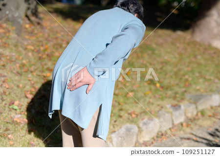 Senior woman complaining of lower back pain, elderly person, lower back pain, buttock pain, worry, anxiety, walking, looking down 109251127