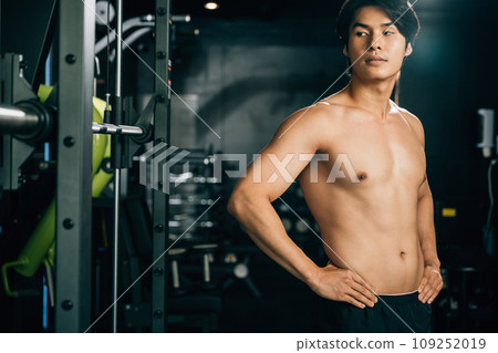 Fit man with strong and toned body, standing in gym interior, works with his coach and trainer to improve his strength and shape, embracing a healthy lifestyle. Healthy fitness with copy space 109252019