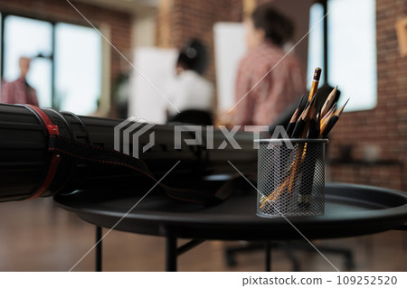 Pencils in metal holder and canvas tube on table in modern art studio, drawing tools and supplies in classroom. People learning to draw and sketch in group, fine arts education 109252520