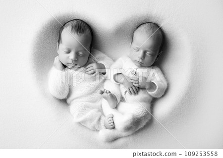 Tiny newborn twin boys in white bodysuits on a white background. Newborn twins sleep next to their brother on the background of the heart. Two newborn twin boys hugging each other. Black and white. Tiny newborn twin boys in white bodysuits on a white background. Newborn twins sleep next to their brother on the background of the heart. Two newborn twin boys hugging each other. Black and white. 109253558