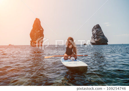 Woman sea sup. Close up portrait of happy young caucasian woman with long hair looking at camera and smiling. Cute woman portrait in bikini posing on sup board in the sea Woman sea sup. Close up portrait of happy young caucasian woman with long hair looking at camera and smiling. Cute woman portrait in bikini posing on sup board in the sea 109254746
