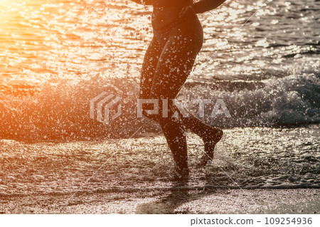 Running woman on a summer beach. A woman jogging on the beach at sunrise, with the soft light of the morning sun illuminating the sand and sea, evoking a sense of renewal, energy and health. Running woman on a summer beach. A woman jogging on the beach at sunrise, with the soft light of the morning sun illuminating the sand and sea, evoking a sense of renewal, energy and health. 109254936