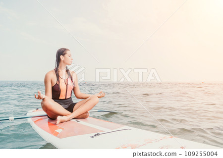 Woman sup yoga. Happy young sporty woman practising yoga pilates on paddle sup surfboard. Female stretching doing workout on sea water. Modern individual female outdoor summer sport activity. 109255004