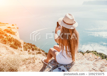 Digital nomad, woman in the hat, a business woman with a laptop sits on the rocks by the sea during sunset, makes a business transaction online from a distance. Freelance, remote work on vacation. Digital nomad, woman in the hat, a business woman with a laptop sits on the rocks by the sea during sunset, makes a business transaction online from a distance. Freelance, remote work on vacation. 109255075