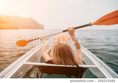 Woman in kayak back view. Happy young woman with long hair floating in transparent kayak on the crystal clear sea. Summer holiday vacation and cheerful female people relaxing having fun on the boat 109255088