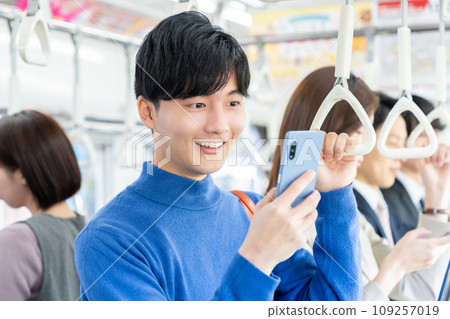 Young college student looking at a smartphone on a train. Photo provided by Keio Electric Railway Co., Ltd. 109257019