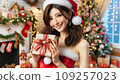 A beautiful Japanese woman is wearing a Santa costume and holding a present. 109257023