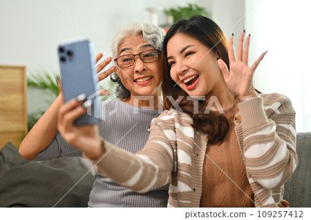 Cheerful young Asian woman taking selfie picture on smartphone with happy mature mother 109257412