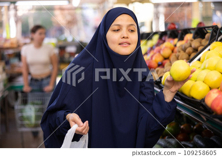 Woman in paranja shopping and choosing local juicy apples in hypermarket 109258605