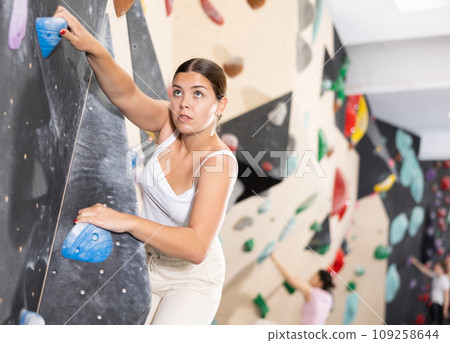 Europian girl focused on climbing to top of artificial bouldering wall along complicated route track 109258644
