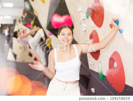 Smiling young girl posing near climbing wall at bouldering gym after workout, feeling accomplished and energized 109258659