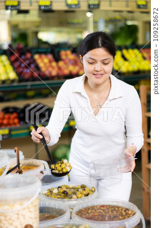 Asian woman puts handful of olives in disposable container with ladle 109258672