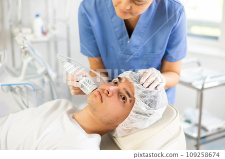 Young woman cosmetologist doing whitening procedure to young man 109258674