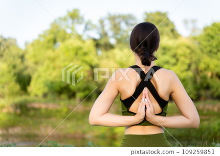 healthy lifestyle with yoga in nature: a girl performing a pose on a summer day joining hands with palms behind her back. close-up healthy lifestyle with yoga in nature: a girl performing a pose on a summer day joining hands with palms behind her back. close-up 109259851