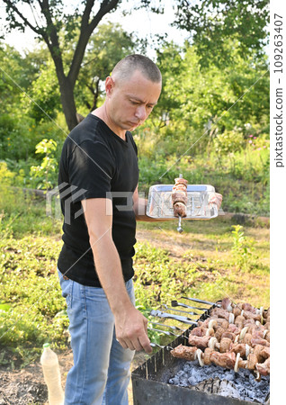 a man smoothes a skewer of a barbecue on the grill a man smoothes a skewer of a barbecue on the grill 109263407