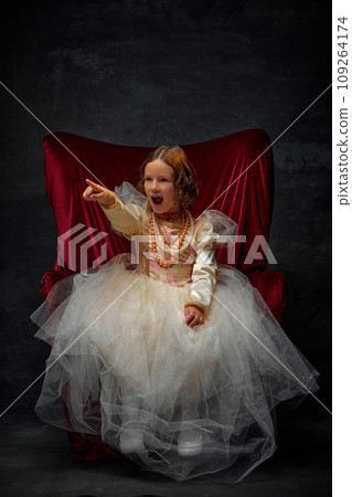 Get out. Little girl sitting on throne wearing in old-fashioned dress like princess and shouting threatening someone against dark vintage background. 109264174