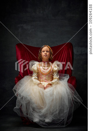 Portrait of little girl, kid dressed like medieval person in old-fashioned dress sitting on throne against dark vintage background. Portrait of little girl, kid dressed like medieval person in old-fashioned dress sitting on throne against dark vintage background. 109264188