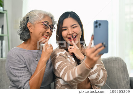 Happy young Asian woman taking selfie picture on smartphone with happy mature mother 109265209