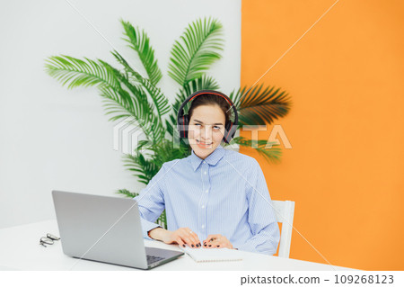 Head shot happy young indian ethnicity female manager wearing wireless headphones, looking at laptop screen, 109268123