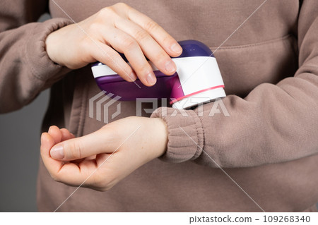 Woman removing pills from clothes with electric portable clothes pill remover Woman removing pills from clothes with electric portable clothes pill remover 109268340