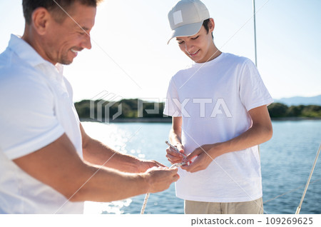 Mature man and his son spending time on the yacht and looking happy 109269625