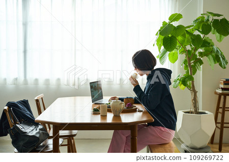 一位女士一邊看著電腦，一邊匆匆吃早餐 109269722