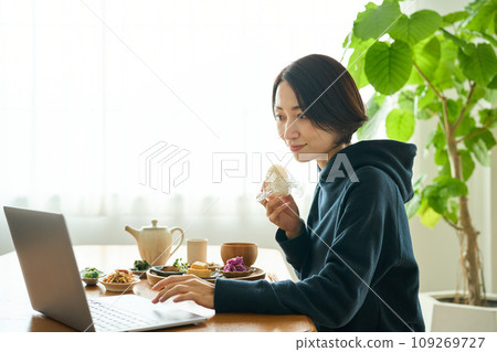 A woman hurriedly eats breakfast while looking at a computer 109269727