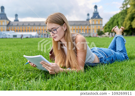 Young student girl lying on grass, educational building background 109269911