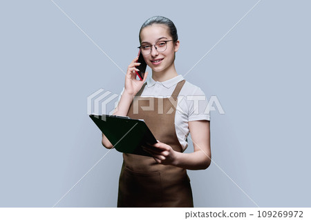Young female worker in apron taking order by phone, writing, on gray background 109269972