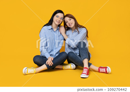 Two sisters are sitting on a yellow background 109270442