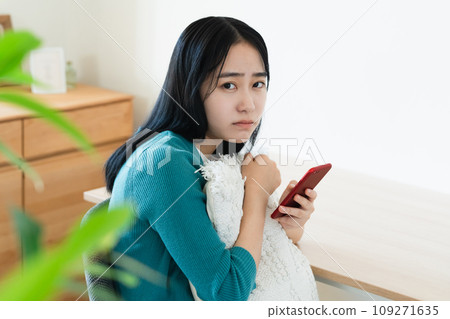 Young woman holding a smartphone and thinking 109271635