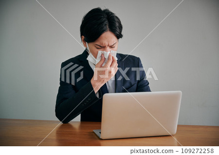 Young male office worker wiping his runny nose with a tissue Young male office worker wiping his runny nose with a tissue 109272258