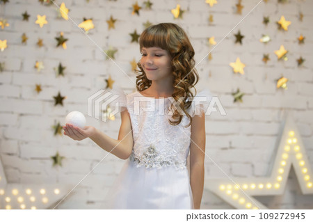 Beautiful child with a Christmas ball. Little model girl in a white dress. Smart girl 109272945