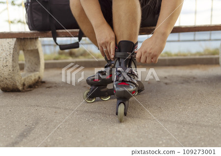 Legs of young man putting on roller skates in the park 109273001