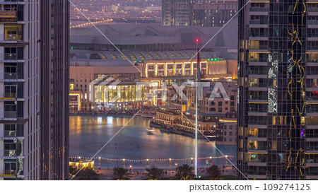 Aerial view of Dubai Fountain in downtown with palms in park next to shopping mall and souq day to night timelapse, UAE 109274125