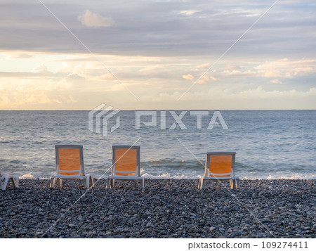 Empty sunbeds on the beach. Seaside chairs. End of beach season. At sunset. Vacation at the resort. 109274411