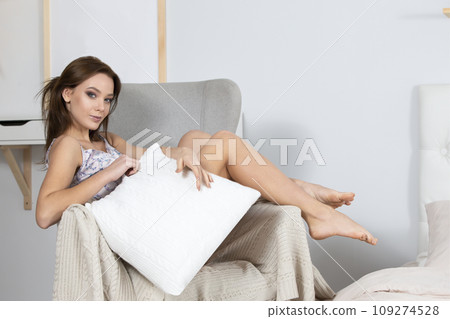 Beautiful girl in pajamas. Luxurious model in home clothes.Young woman in home clothes is sitting in a chair with a pillow 109274528