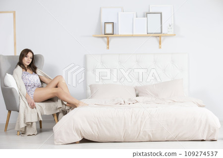 Girl in pajamas sits in a chair in a bright bedroom Girl in pajamas sits in a chair in a bright bedroom 109274537