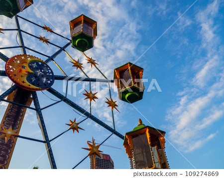 A small Ferris wheel in the park. A bright attraction for children. Entertainment in the park. Colorful booths. High above the ground. Children's fun. Entertainment industry concept. A small Ferris wheel in the park. A bright attraction for children. Entertainment in the park. Colorful booths. High above the ground. Children's fun. Entertainment industry concept. 109274869