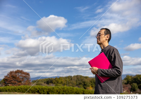 Mature man standing outdoors holding a pink file 109275373