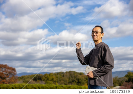 Mature man standing outdoors with a tablet Mature man standing outdoors with a tablet 109275389