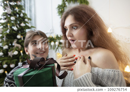 Receive a gift. An enthusiastic woman received a Christmas surprise. Christmas couple. Open the christmas box. Emotion surprise Receive a gift. An enthusiastic woman received a Christmas surprise. Christmas couple. Open the christmas box. Emotion surprise 109276754
